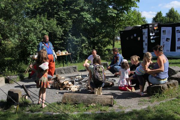Gruppe von Erwachsenen und Kindern, die um ein Lagerfeuer sitzen und Stockbrot essen