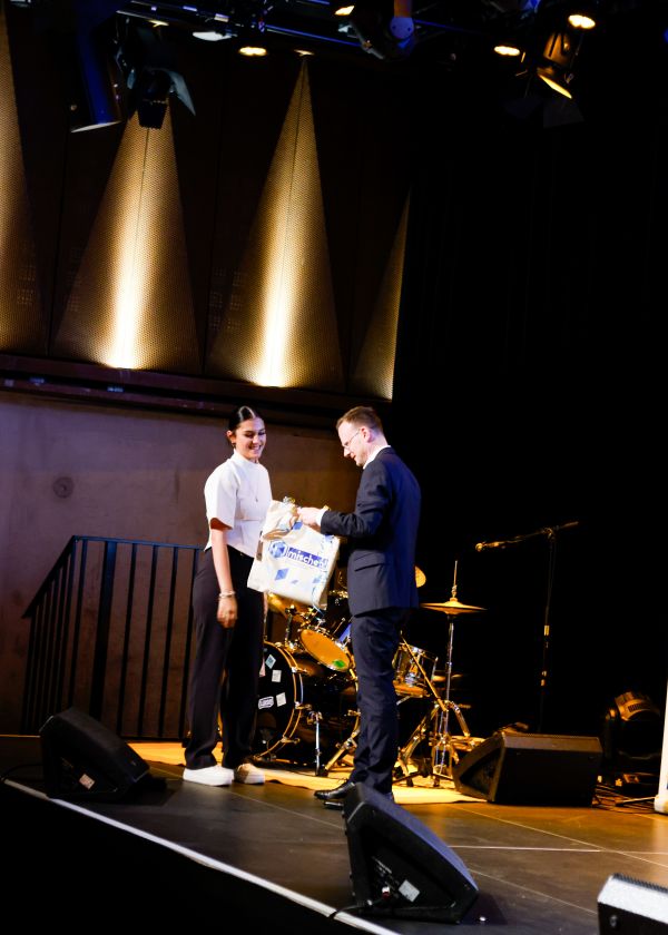 Übergabe des Gruppenpreises der Mitmachaktion. Ein Mann reicht einer Frau eine mischen!-Stofftasche mit Geschenkschleifen.