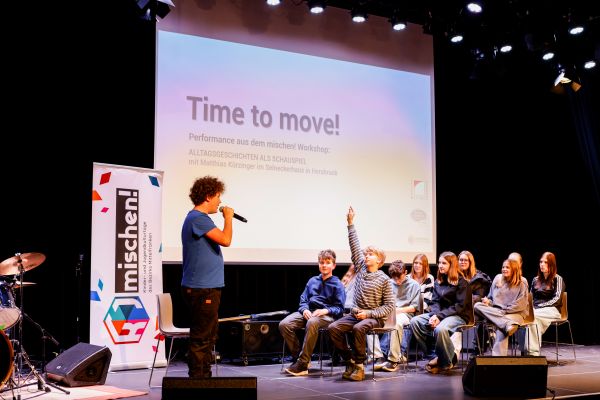 Jugendliche auf der Bühne. Im Hintergrund ist auf der Präsentation zu lesen: Time to move! - Performences aus den Workshops