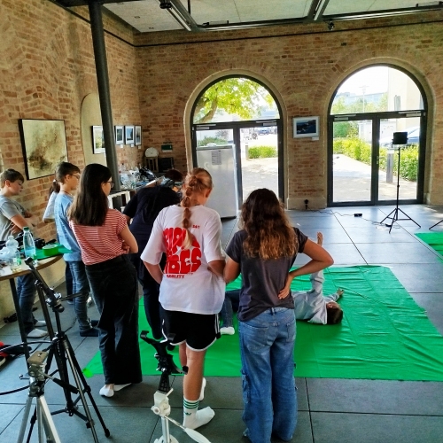 Jugendliche stehen in einem großen Saal hinter der Kamera. Vor der Kamera sind Greenscreens aufgebaut und es wird performt.