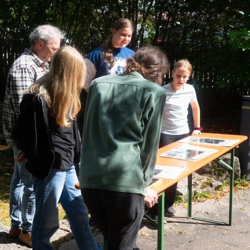 Jugendliche die sich draußen befinden betrachten ihre Bilder, die auf einem Biertisch ausgestellt sind.