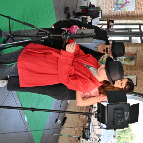 Drei Jugendliche stehen zwischen Scheinwerfern und Greenscreen hinter einer Kamera. Beide sind verkleidet, tragen Hüte, Brillen, Fake-Schnurrbart