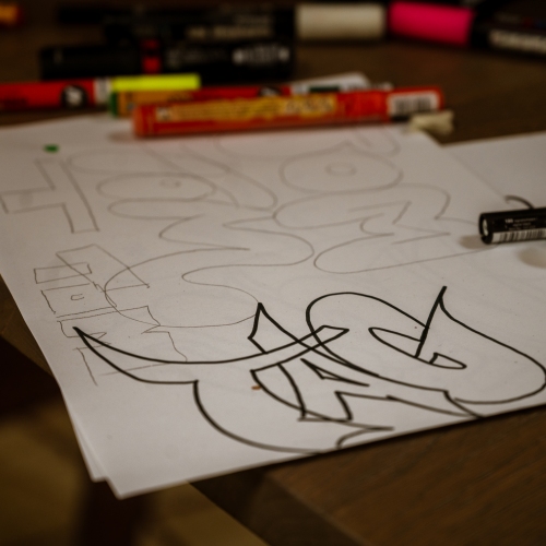 Stifte und ein Papier mit Skizzen und einem TAG-Schriftzug in Graffitistil.