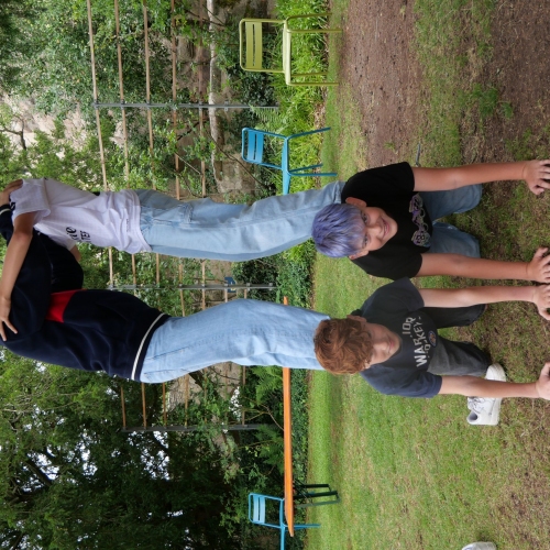 Vier Jugendliche Jungs bilden eine Menschenpyramide. Zwei stehen auf den Rücken der beiden unteren und reichen sich die Hände sodass ein Tunnel entsteht